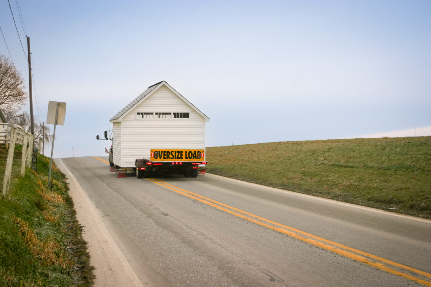 A prefabricated fully-assembled garage being delivered on an oversize load truck