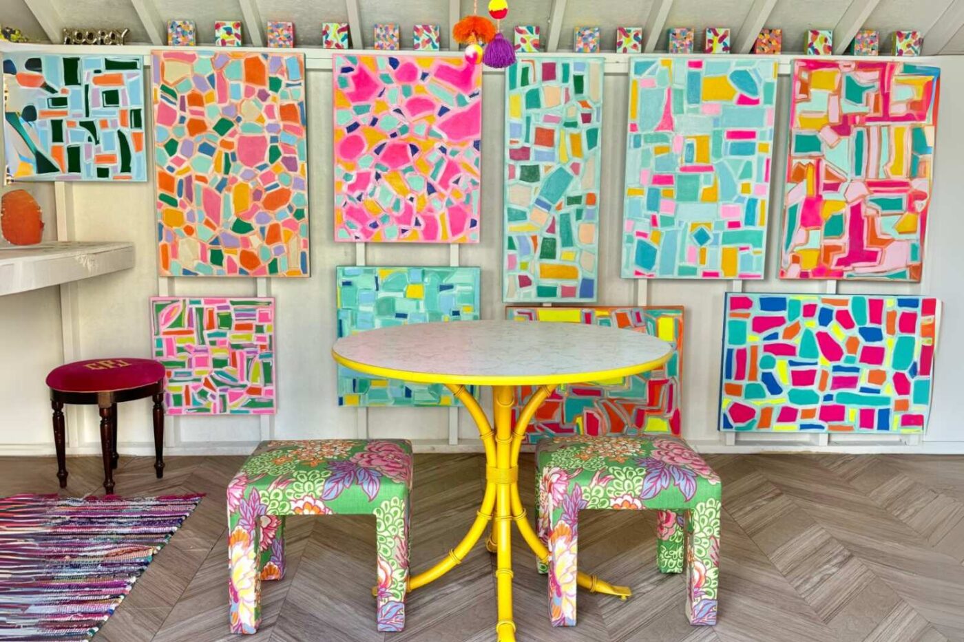 View of small table inside shed with many colorful paintings on the back wall