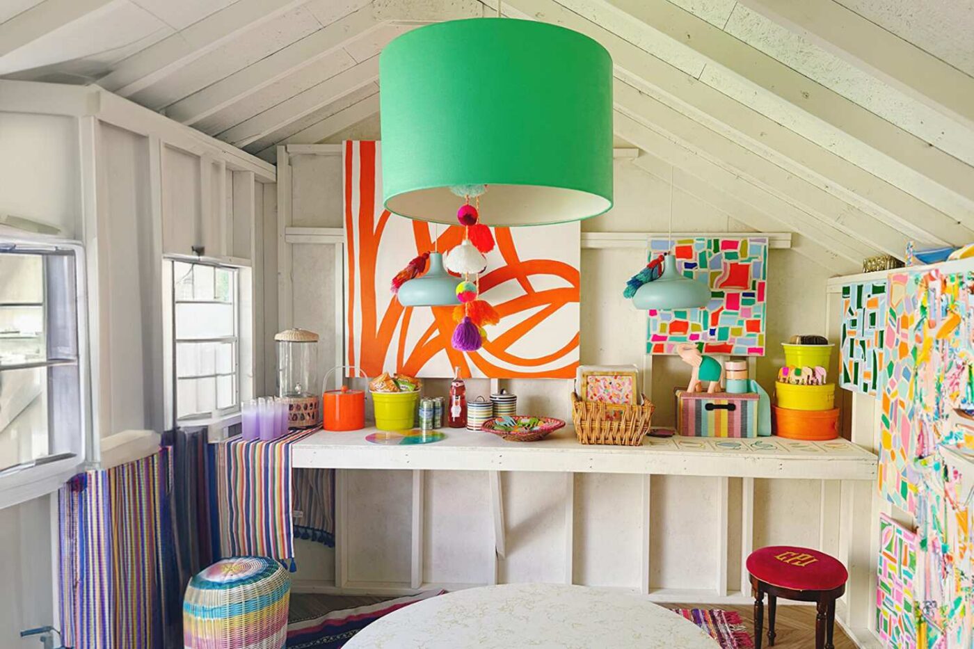 View or workbench in 10x14 Art Studio NY Shed, green light fixture with colorful paintings, white walls, and red stool